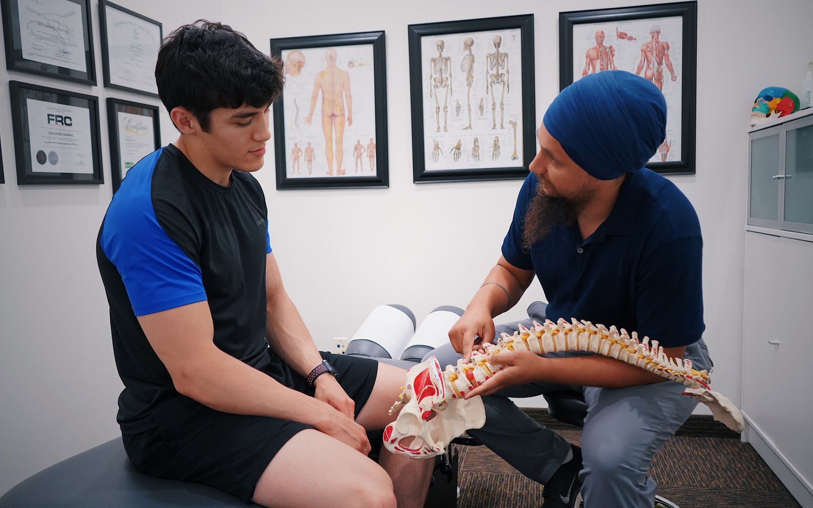 A chiropractor reviewing a spine model with a patient in the exam room